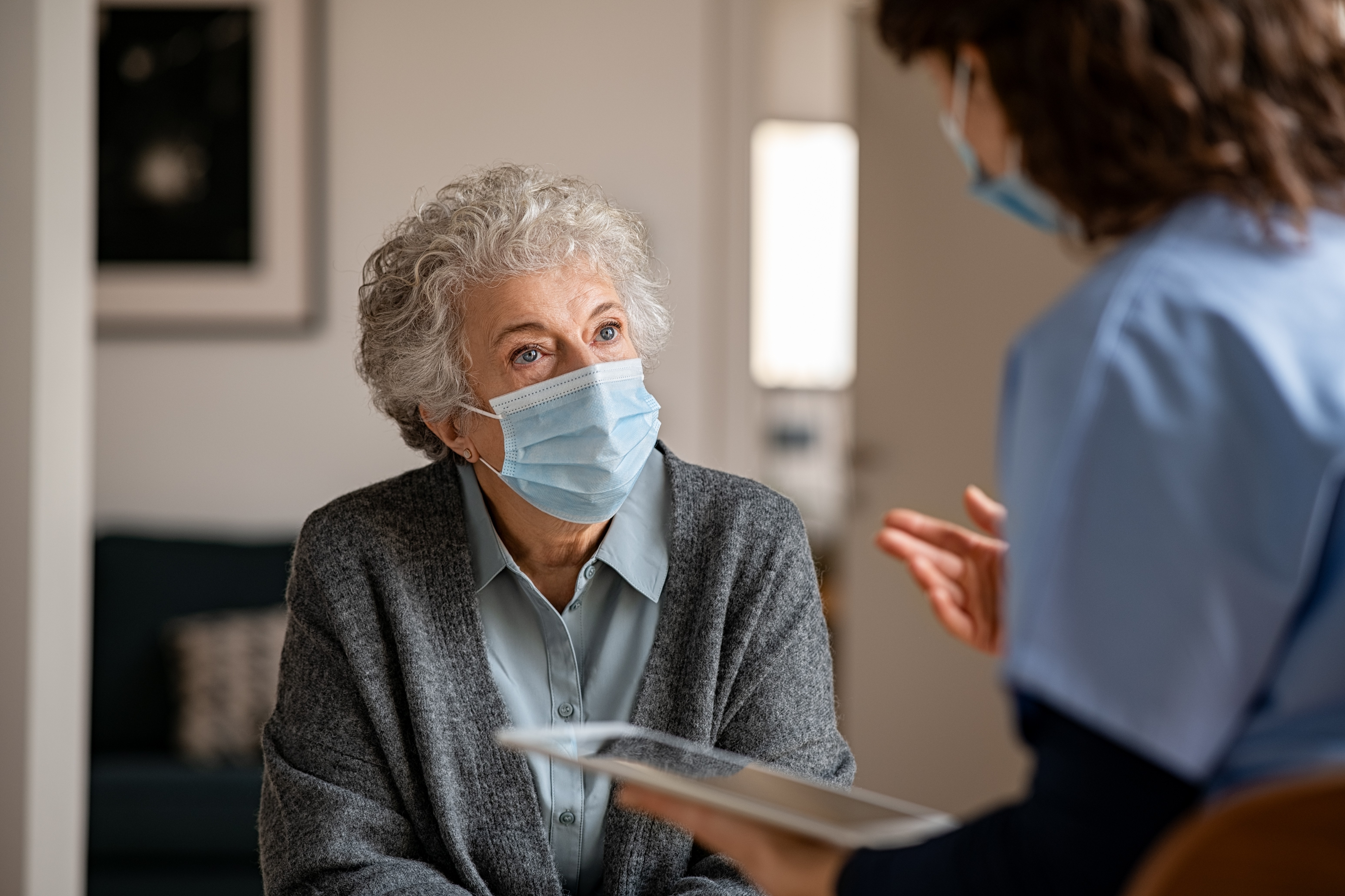 Senior woman wearing a face mask talking to a nurse.