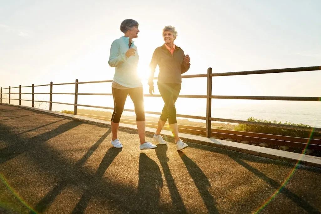 Shot of two women walking together in morning with sun shining from behind.