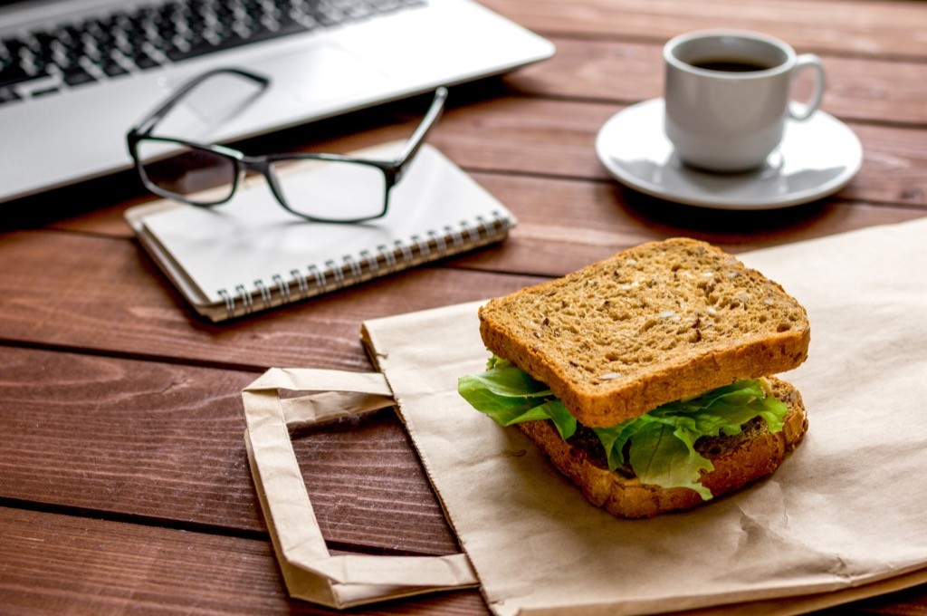 A sandwich for lunch on a brown bag on a desk.