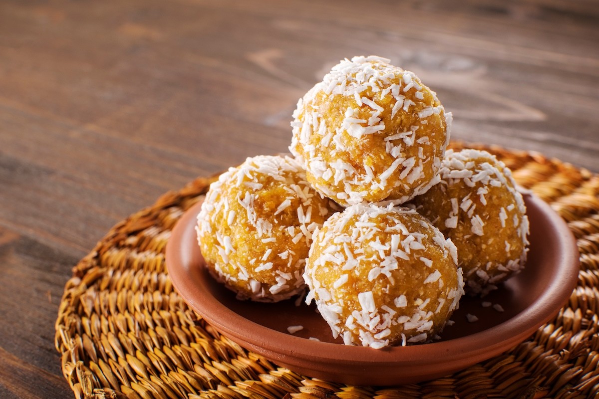 Protein balls with coconut flakes in a terra cotta bowl on a rattan place mat on a wood table