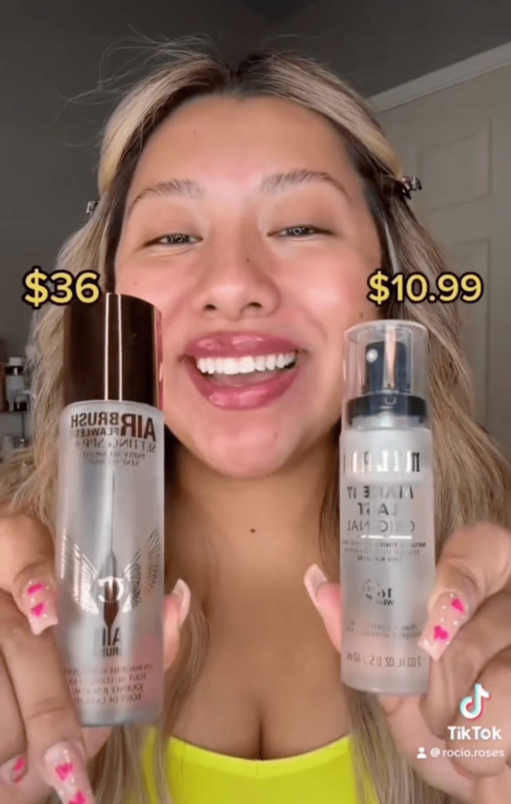 Woman in yellow tank holding up two different bottles of makeup setting spray