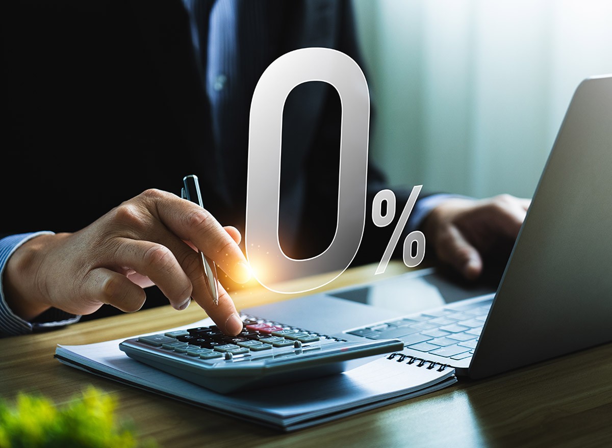 A man using a calculator and laptop behind a 0% symbol.