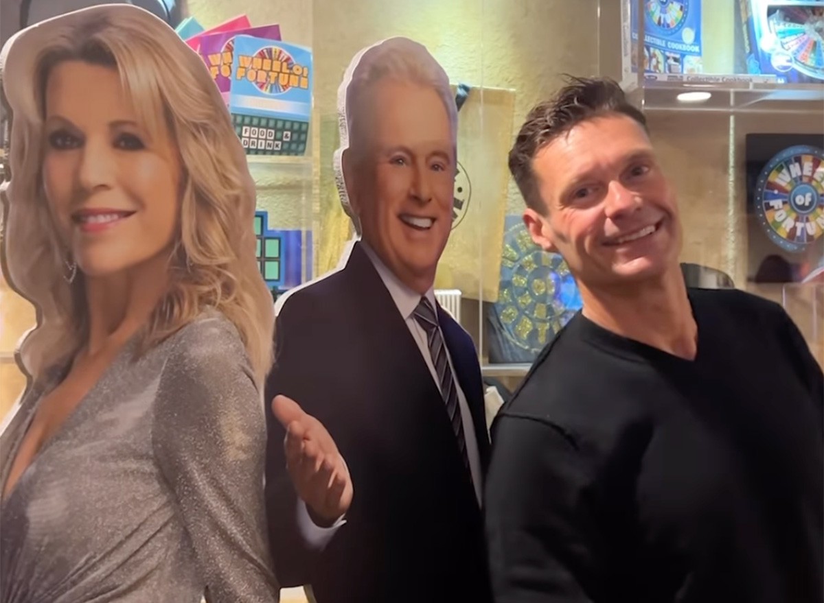 Ryan Seacrest standing in front of a cardboard cut-out of Vanna White and Pat Sajak