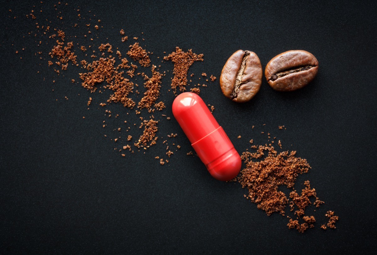 A caffeine pill on a black background, with coffee beans and grounds.