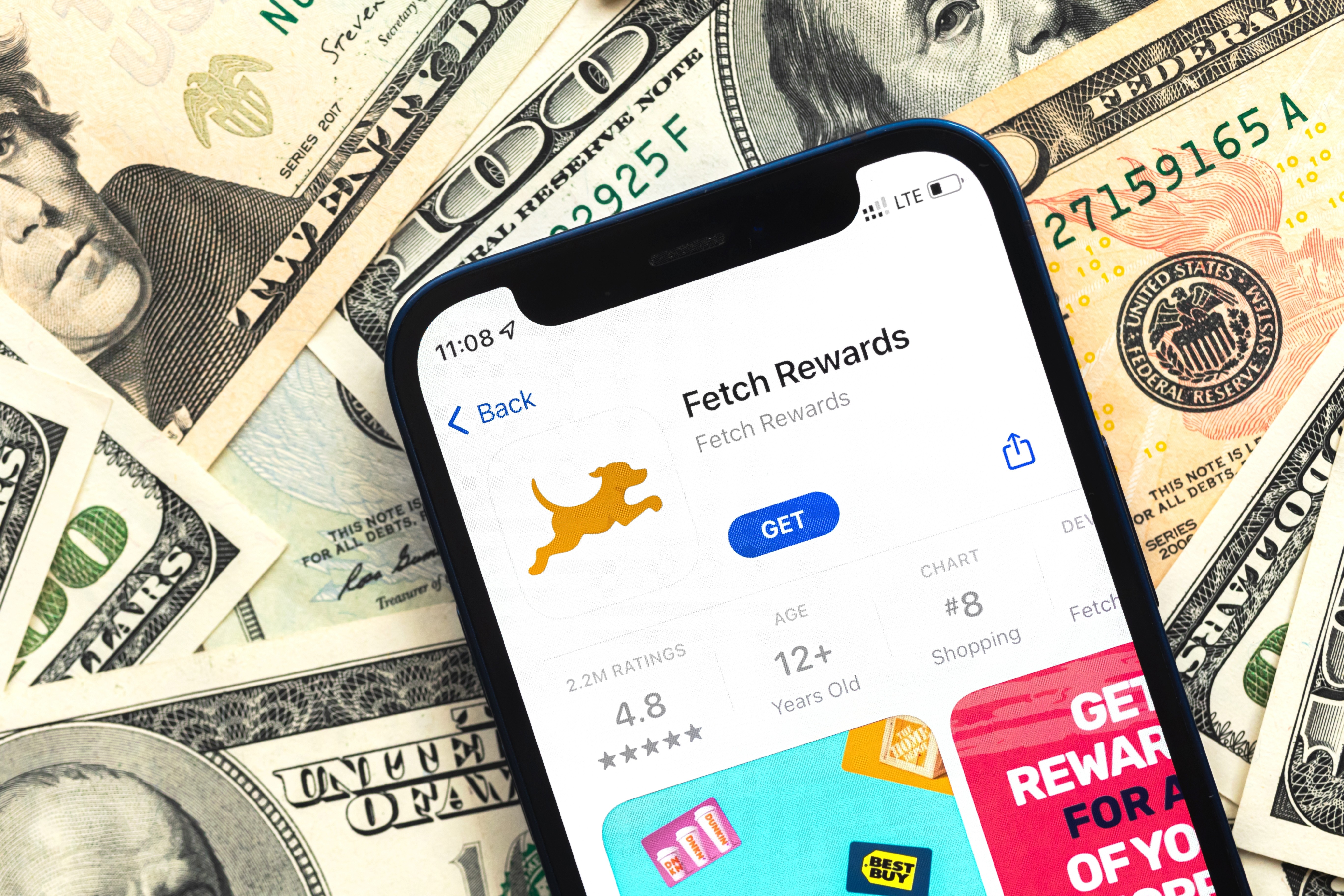 A phone with the Fetch app open on the home screen sits on a pile of cash.