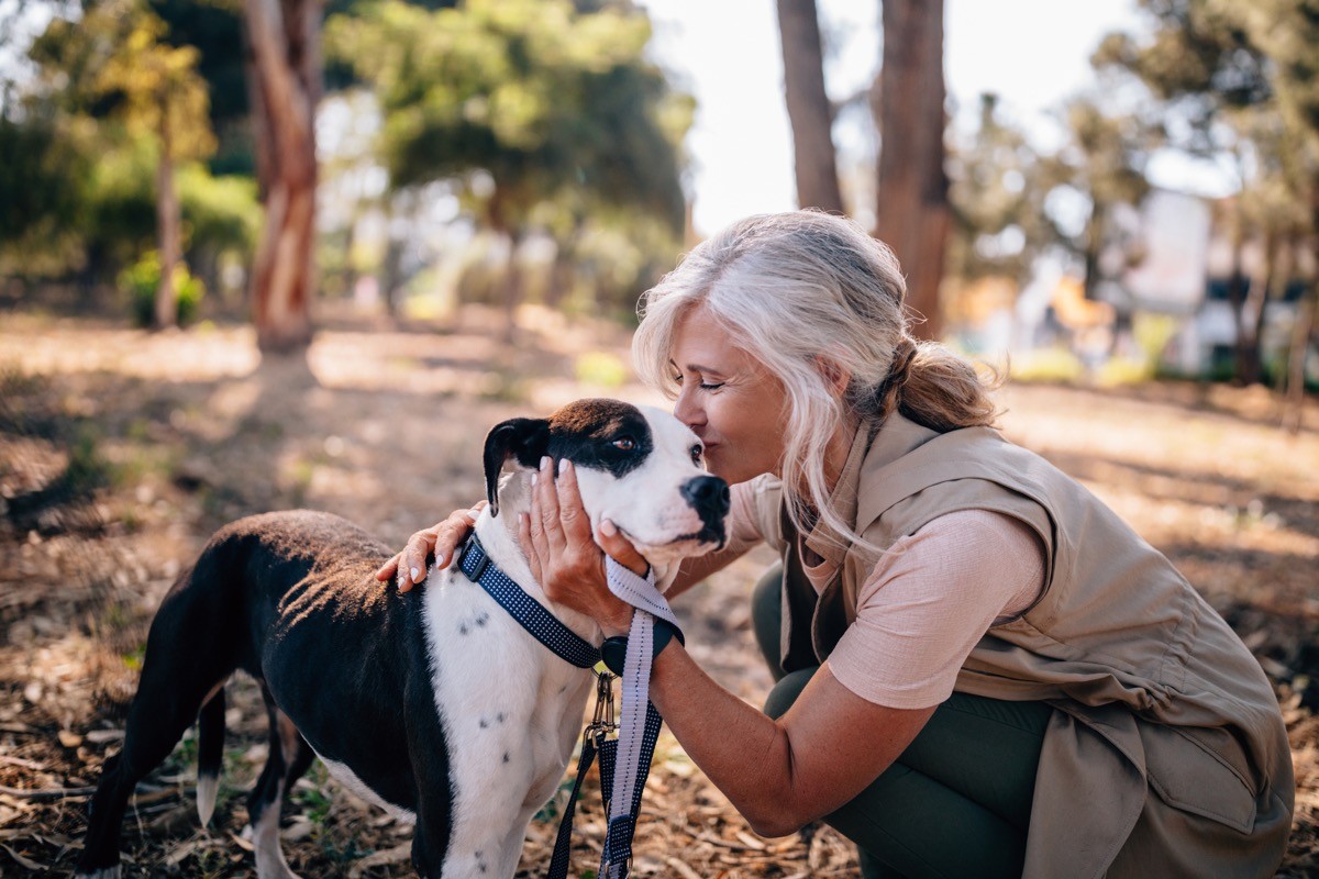 A woman enjoying afternoon walk in park and kissing pet dog on leash.