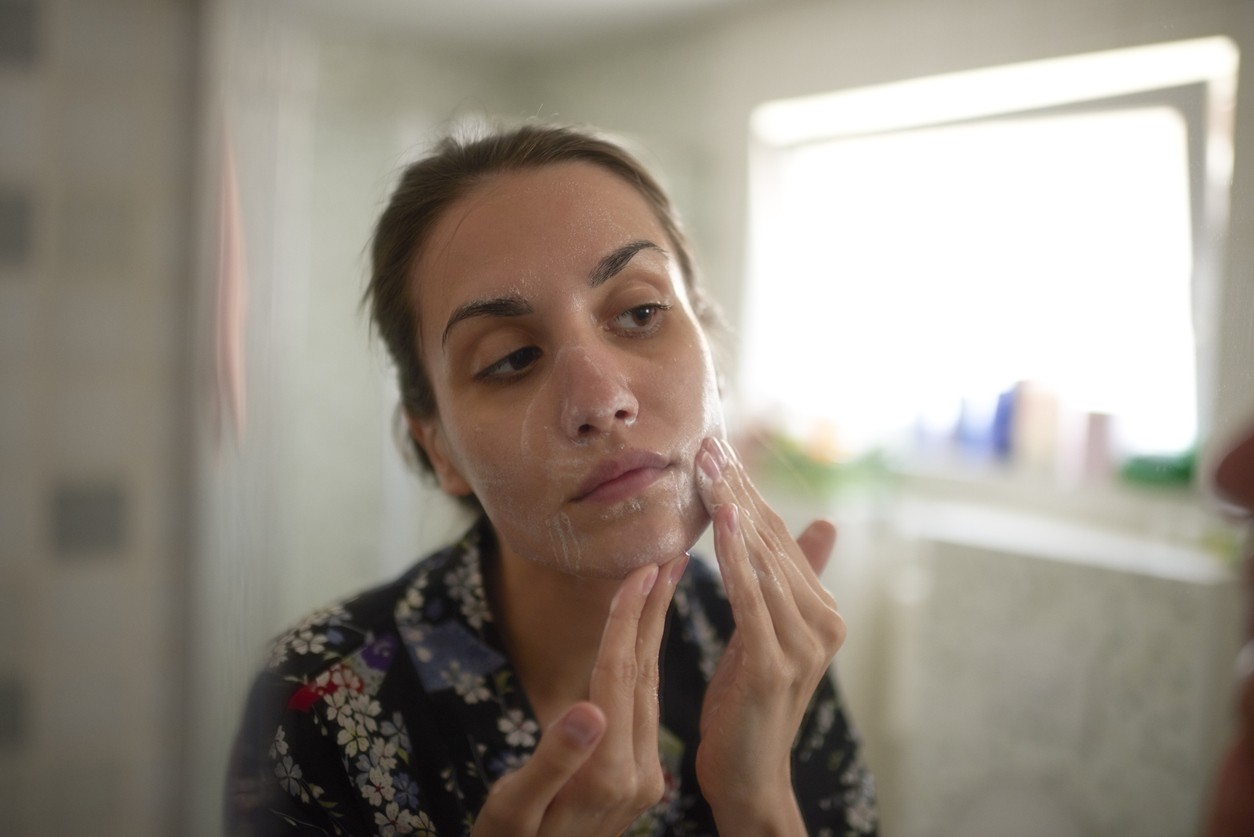 Woman washing her face and looking at her skin in a mirror