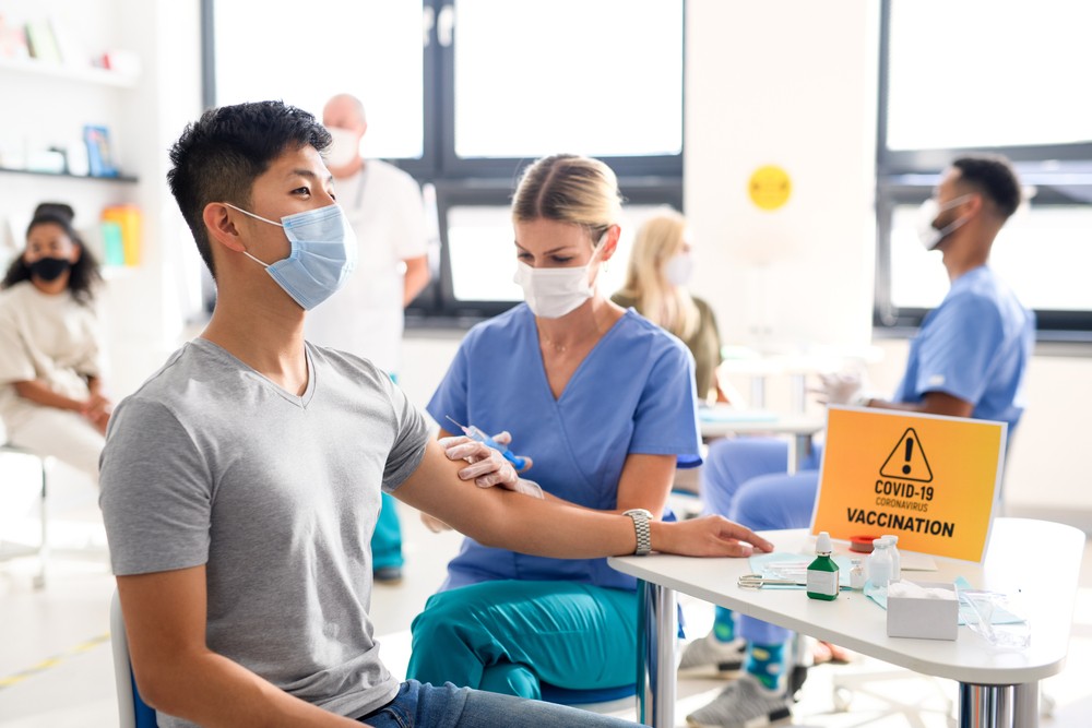 A young man wearing a face mask receives a COVID-19 vaccine from a female doctor in a vaccination center.