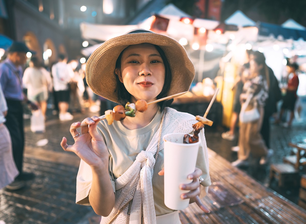 Woman holding bbq grilled skewers at outdoor vendor night market