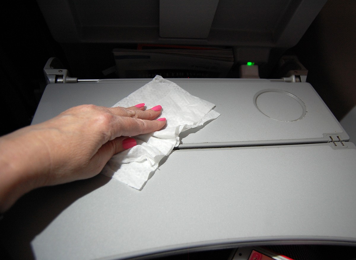 A woman's hand wipes an airplane tray table with a disinfecting wipe.