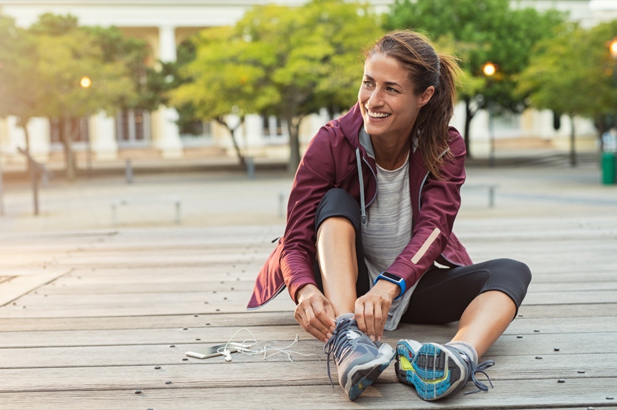 Cheerful woman sitting on the ground tying her shoe laces before a walk