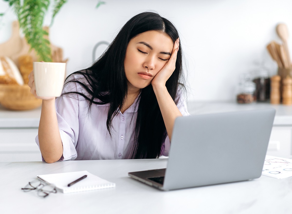 A woman looking tired at her computer holding coffee