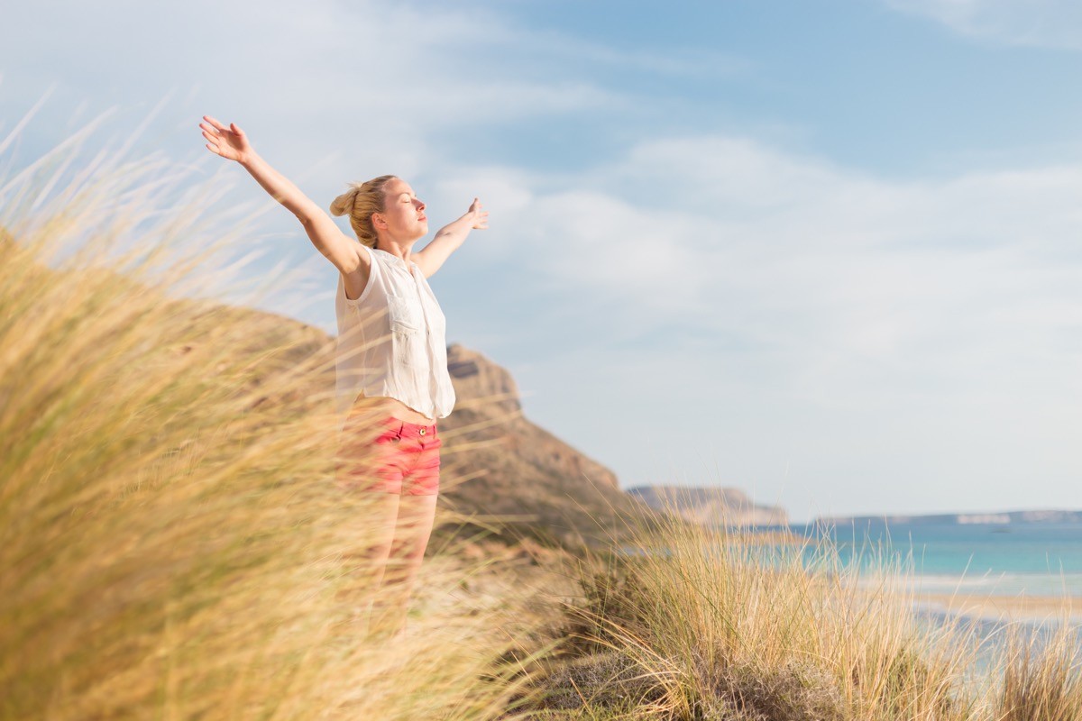 Relaxed woman, arms rised, enjoying sun, freedom and life an a beautiful beach. Y