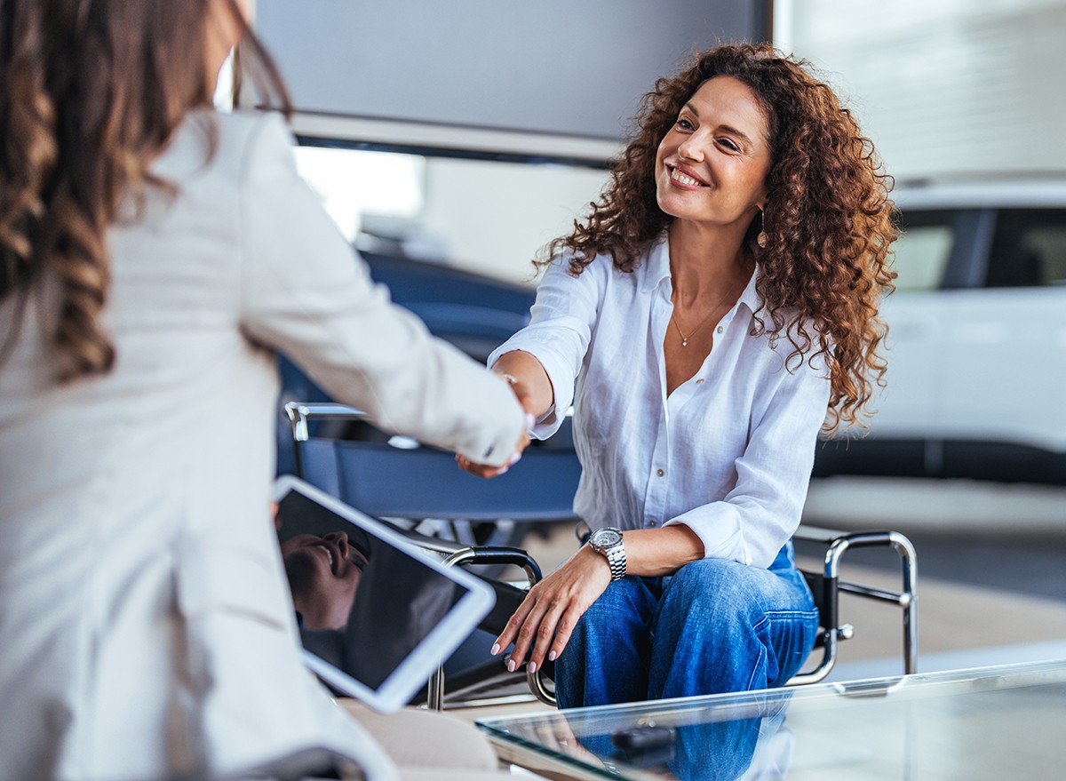 A woman shakes a dealer's hand at a car dealership