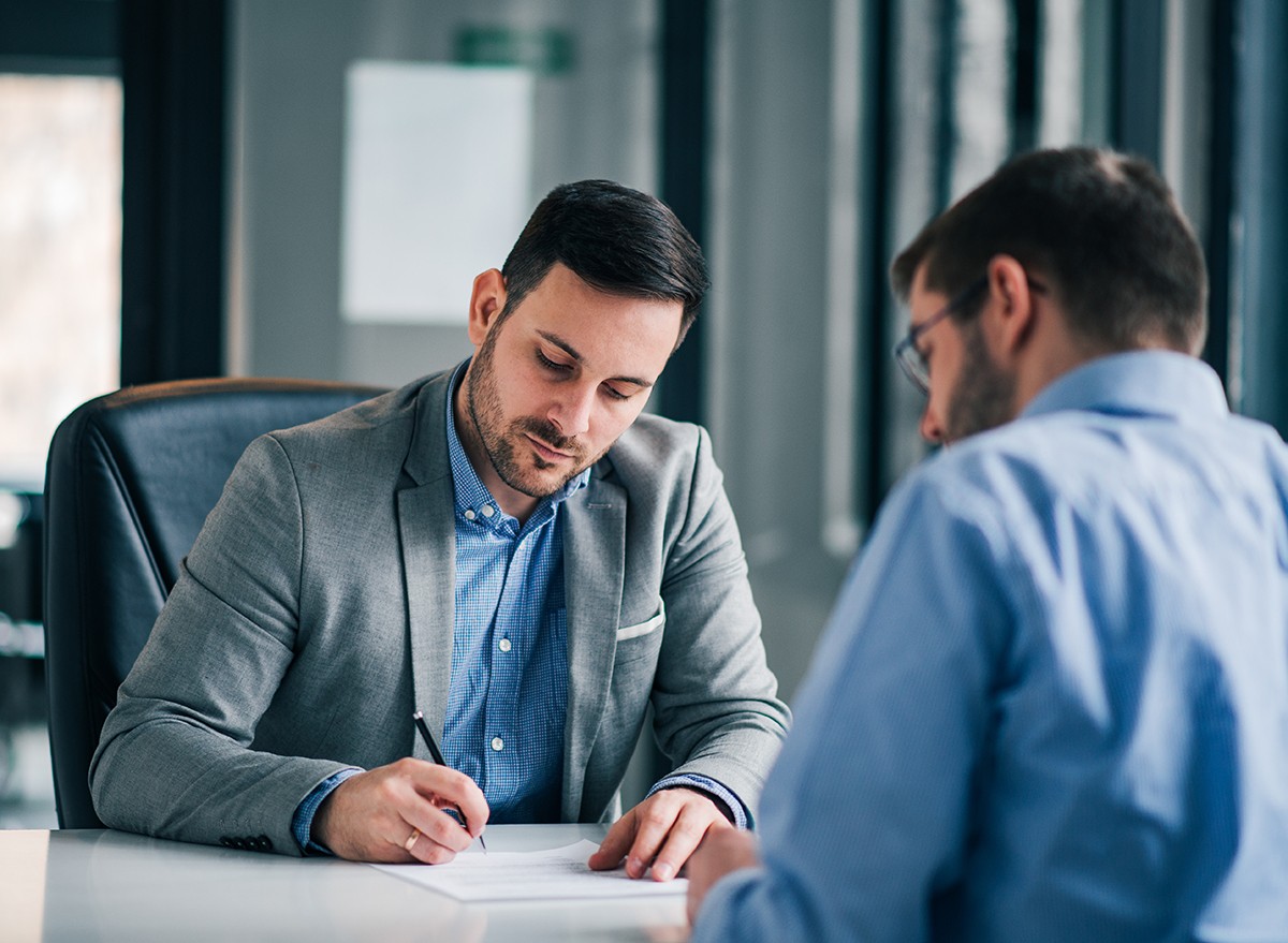 A salesman draws on paper in front of a client sitting at a desk