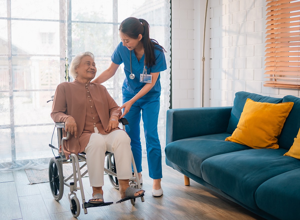 A senior woman in a wheel chair is attended to by nursing home staff