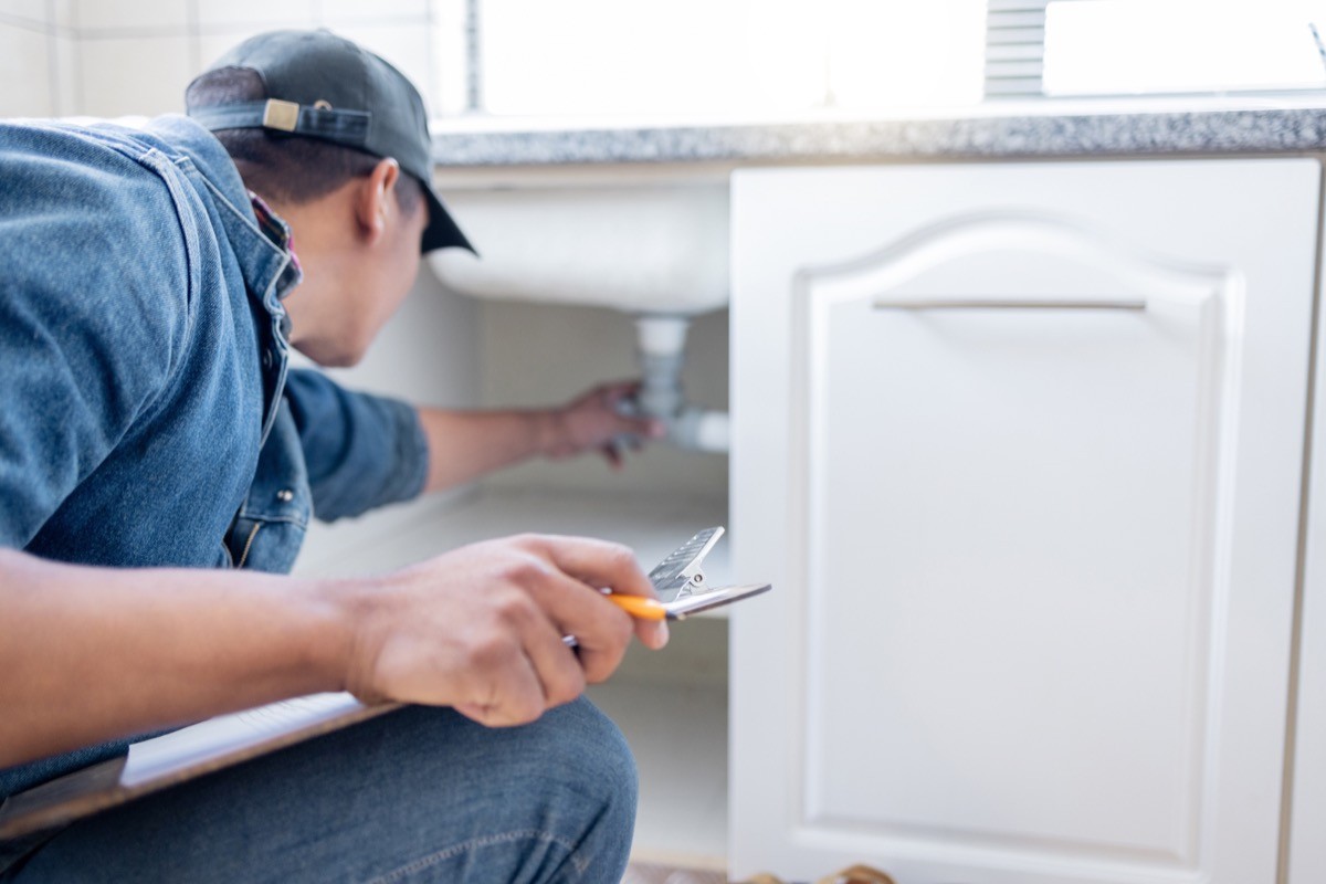 A contractor inspects plumbing under a sink