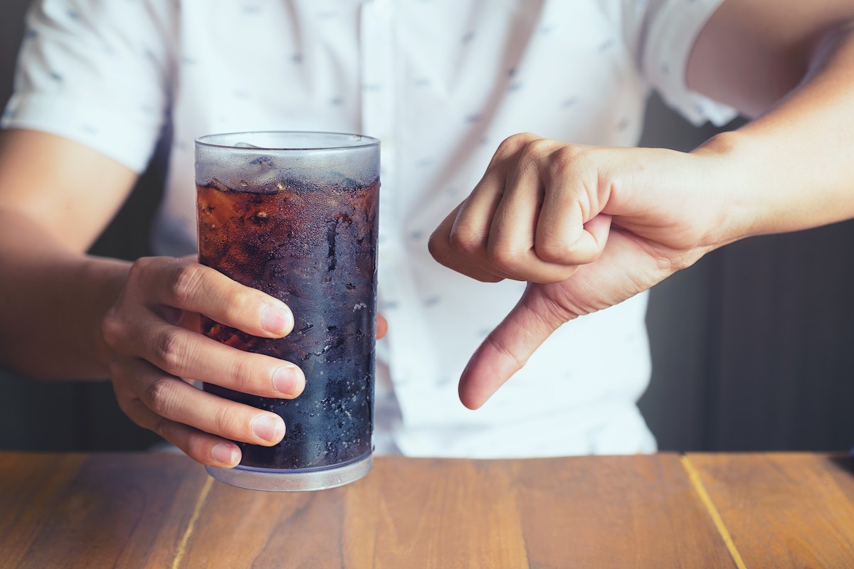 Person holding glass of soda and give it a thumbs down