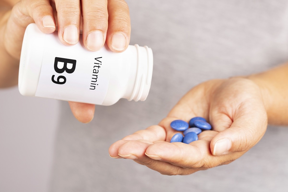 closeup of a person holding a bottle of vitamin B9 supplements and putting the blue pills in their hand