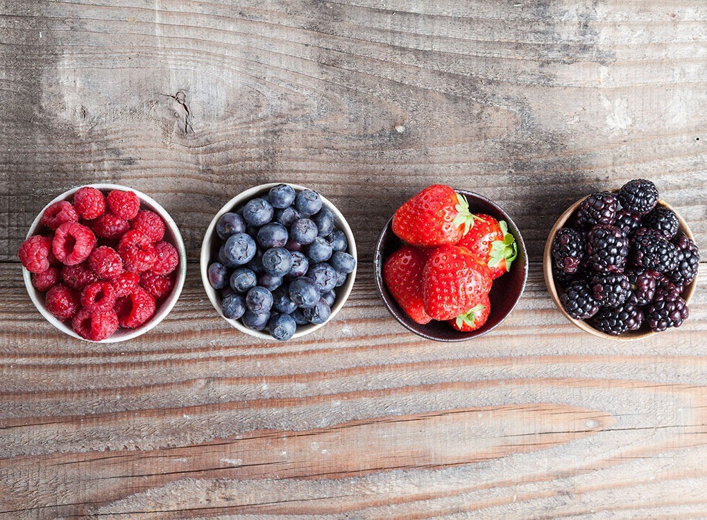 berries lined up in small bowls on wooden table