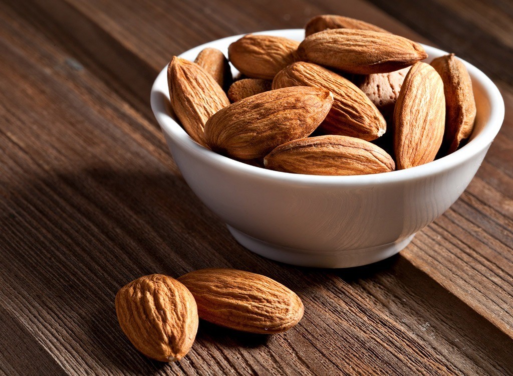 Almonds in a small white bowl on a wood surface