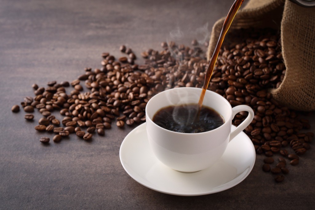 coffee being poured into a mug that's on a counter with coffee beans