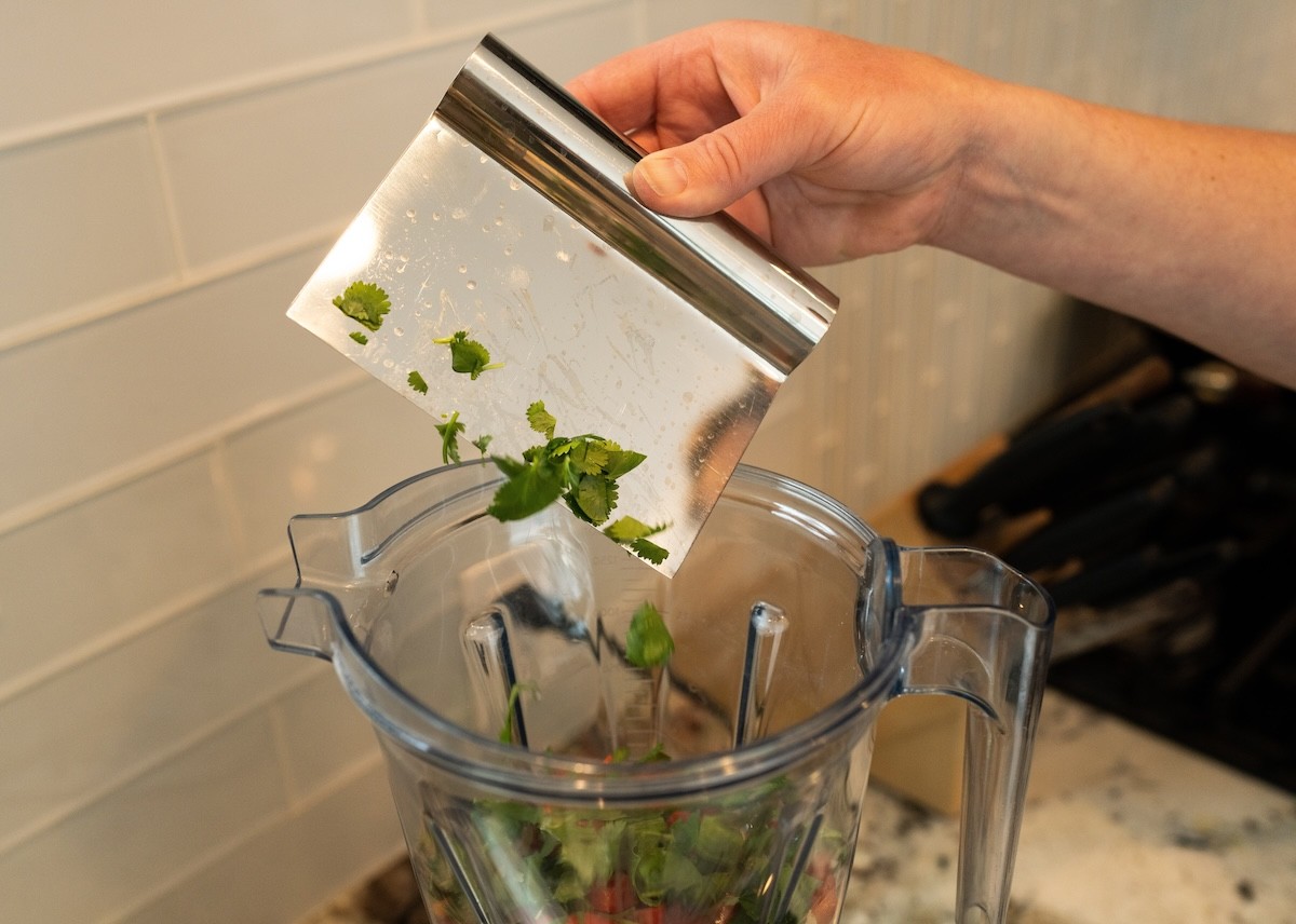 adding herbs to blender with bench scraper