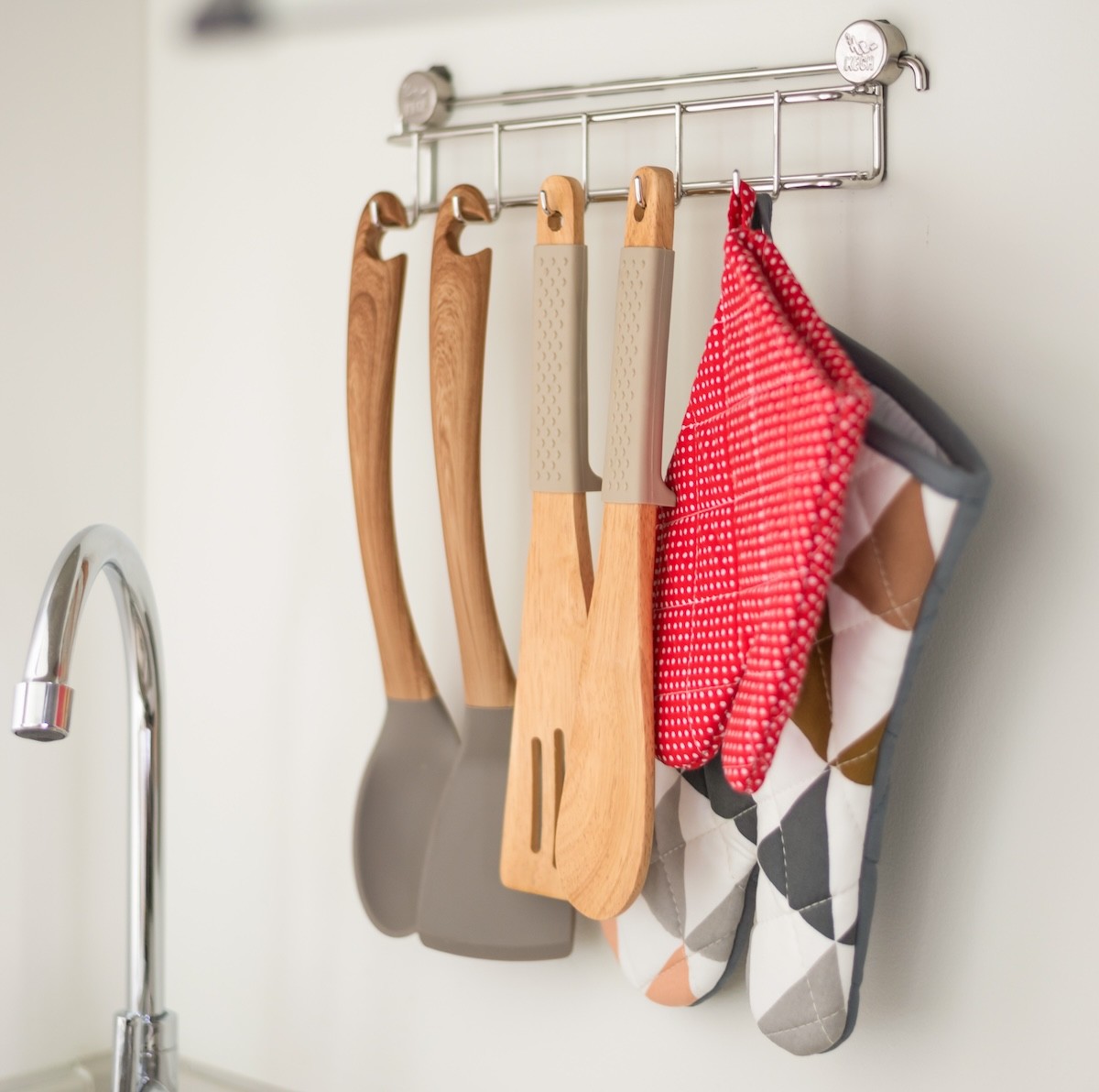 Kitchen utensils and oven mitts hanging on hooks next to a sink
