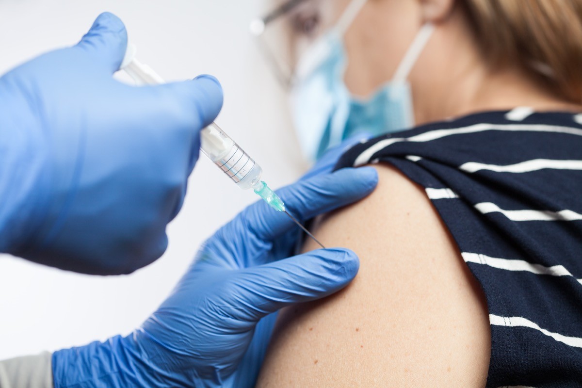 Closeup of medical worker's hands in blue protective gloves injecting vaccine booster shot into elderly patient's shoulder