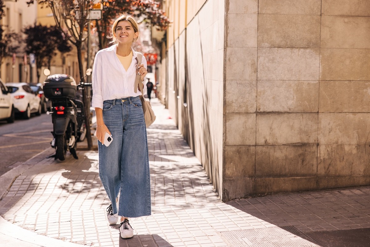 woman walking down old city sidewalk wearing wide-leg jeans and a white blouse