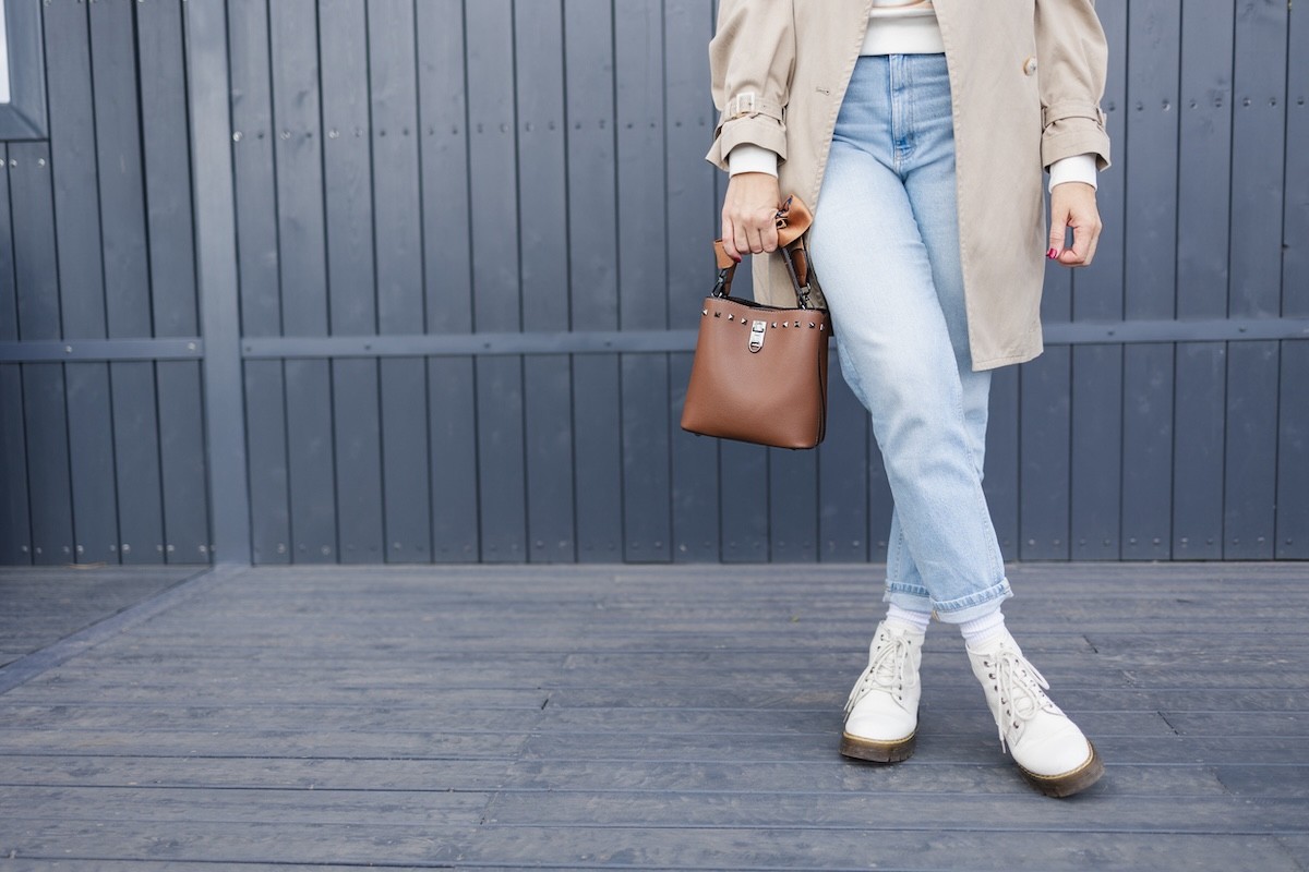 waist-down view of woman wearing light-wash boyfriend jeans, off-white boots and a beige jacket