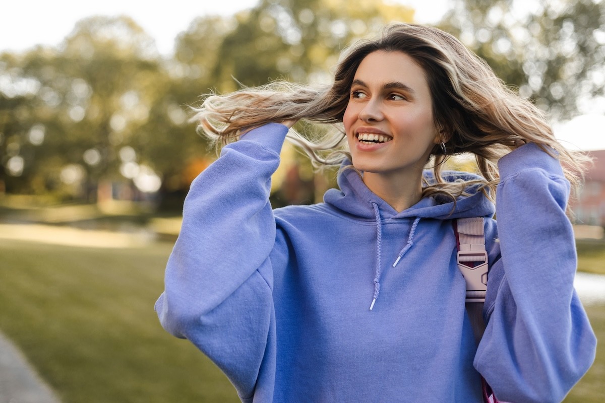 woman with long blonde hair wearing a periwinkle sweatshirt standing outside