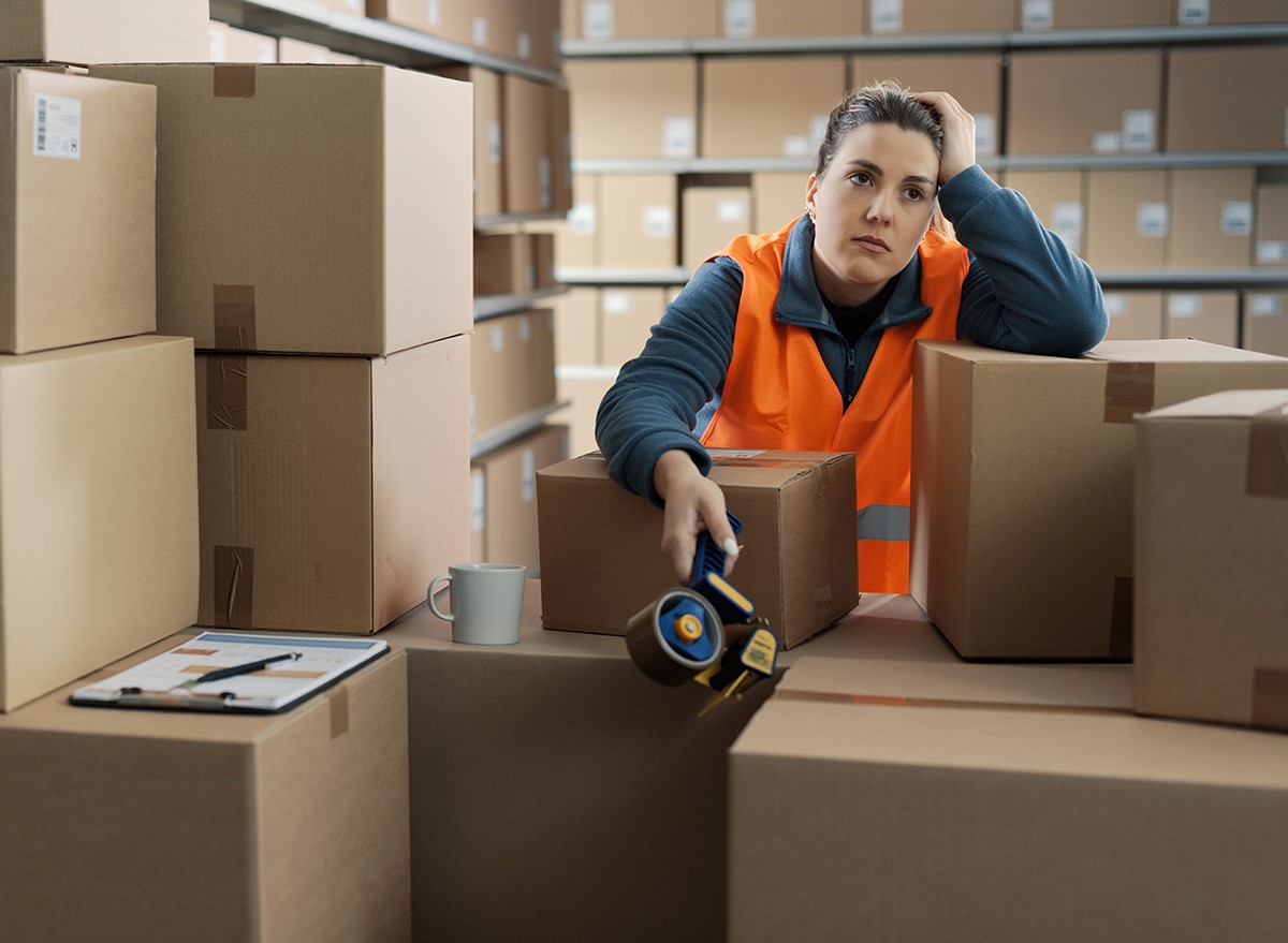 A woman working in shipping takes a coffee break amongst piles of boxes