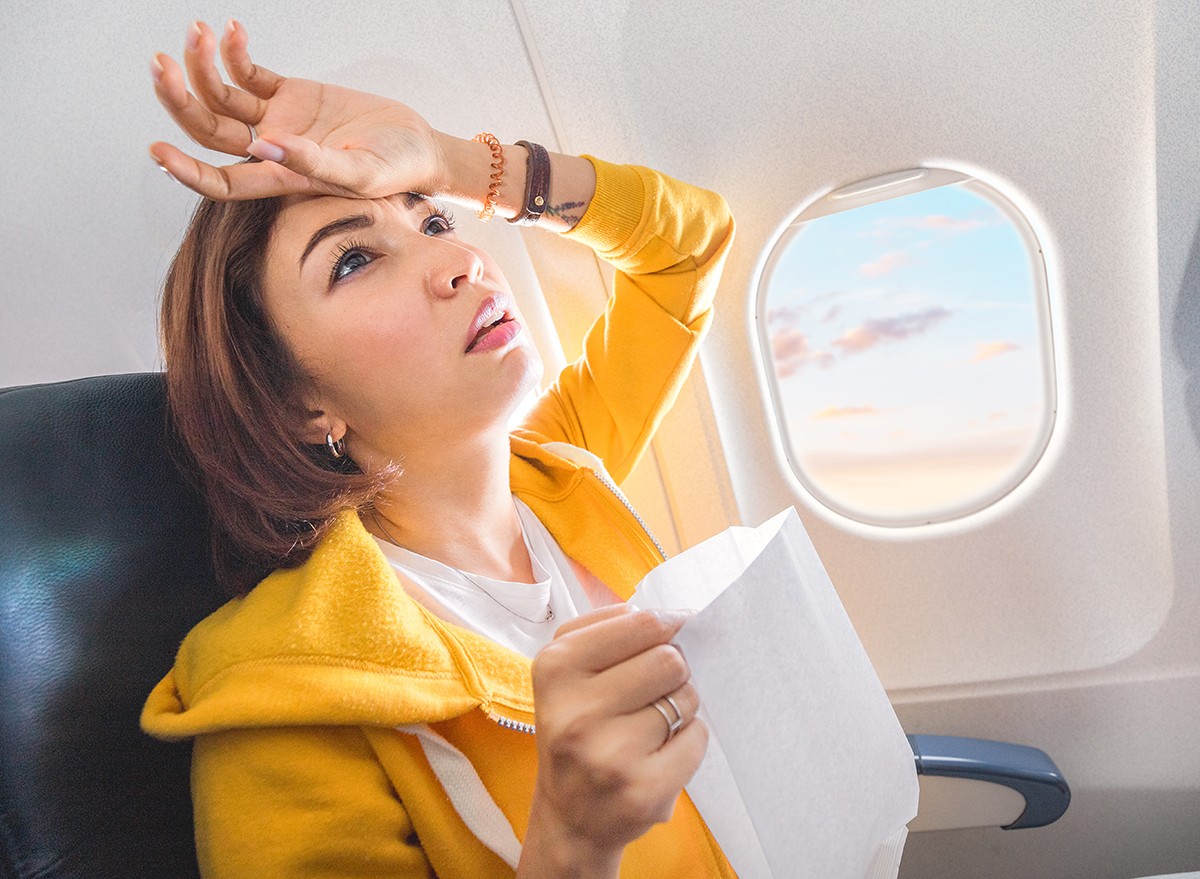 A woman holding an air sickness bag looks unwell on a flight