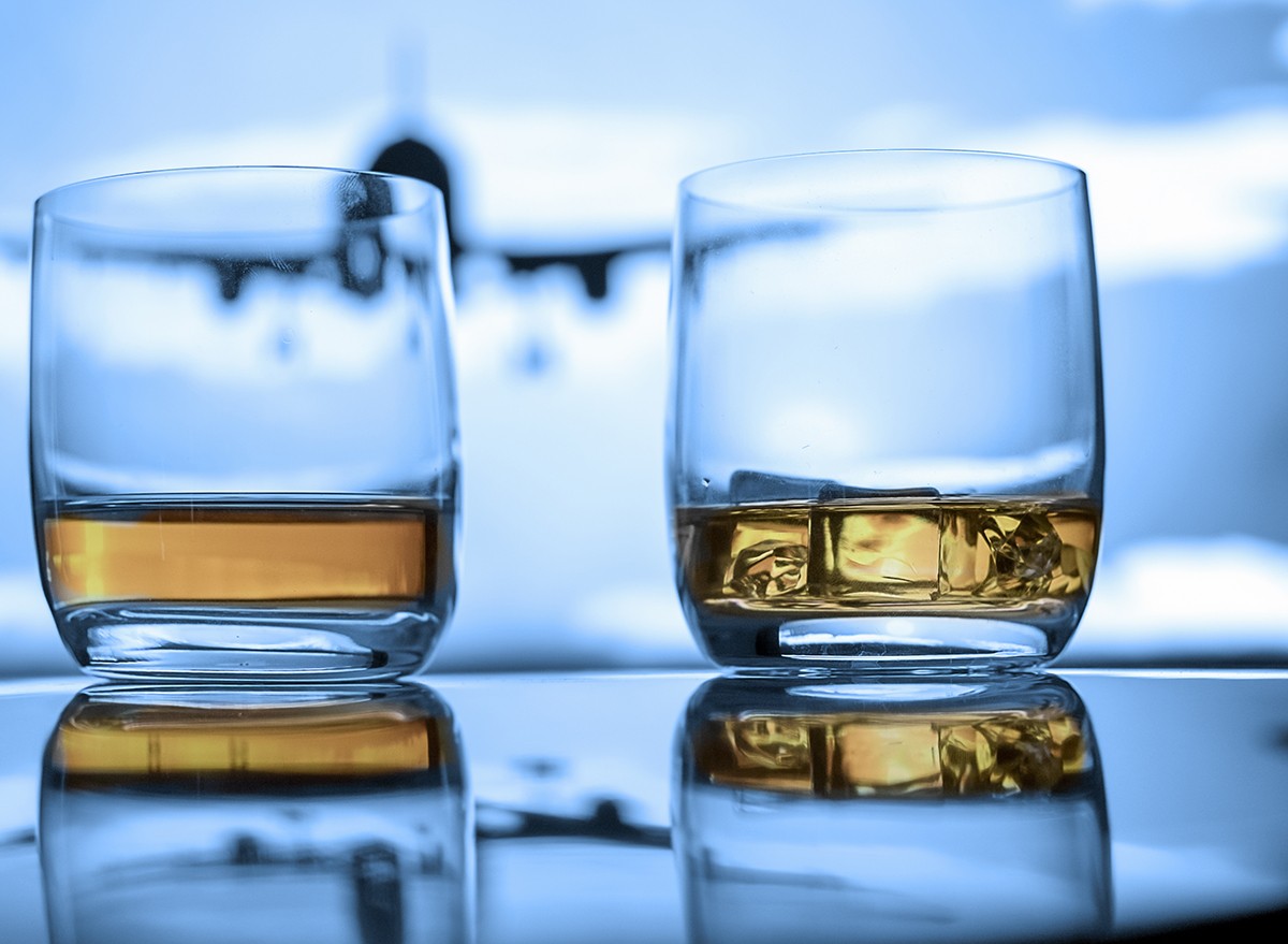 Two glasses of alcohol in a window with an airplane in the sky in the background