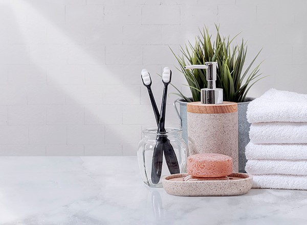 Toothbrushes, soap, hand soap and folded white towels on a bathroom vanity