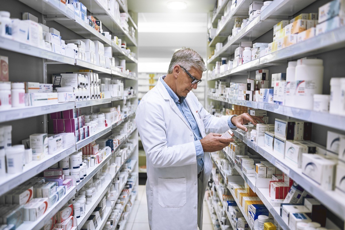 A focused pharmacist making notes of the medication stock on the shelves in a pharmacy