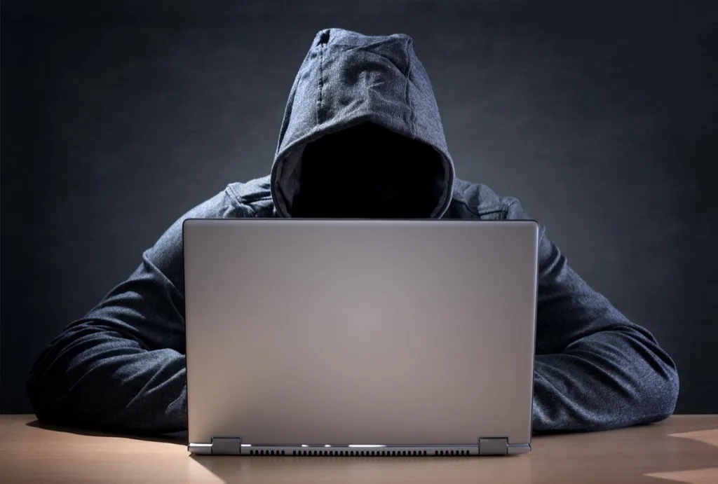 A hacker wearing a hoodie sits in front of an open laptop
