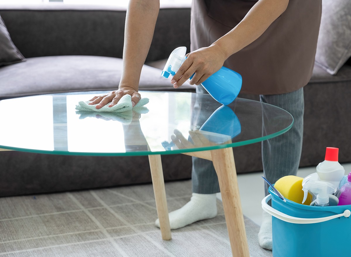 A woman cleaning a glass table uses rubbing alcohol and white vinegar in a spray bottle