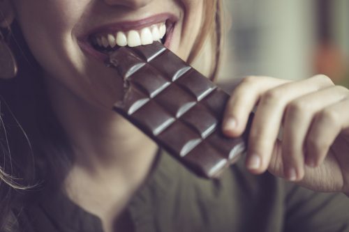 closeup of a smiling woman eating a bar of dark chocolate
