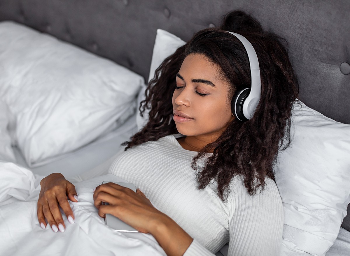 A woman in bed uses an app for sound frequency therapy to help her fall asleep