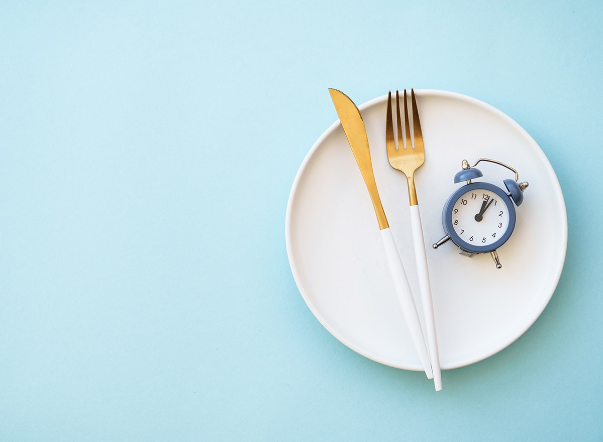 Empty plate, fork and knife, and an alarm clock on blue background