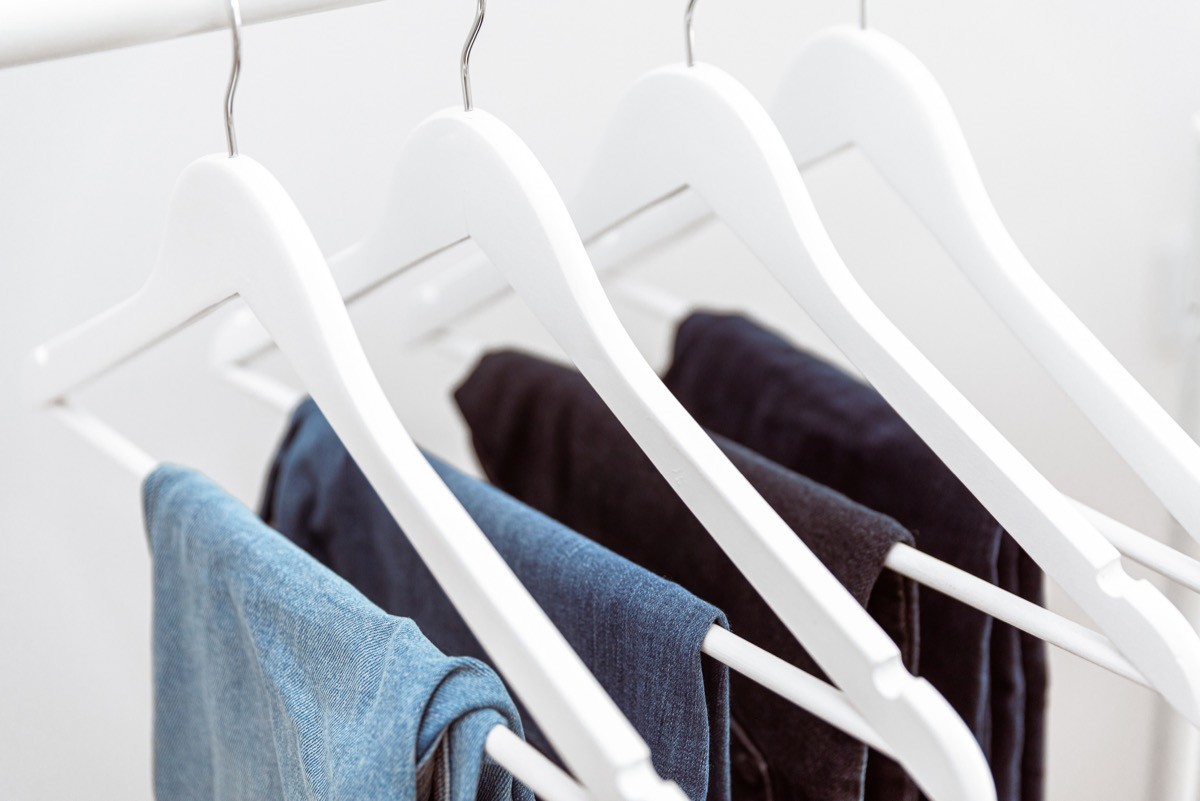 Many blue denim jeans hanging on white clothes hangers on clothing rack