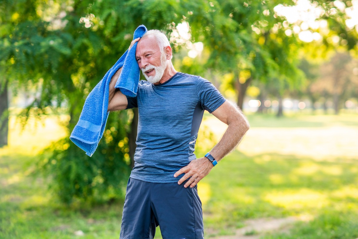 Senior man with white hair and beard wearing blue workout clothes takes a break while exercising outside in the morning
