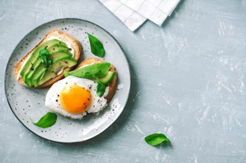 Sliced avocado and egg on toasted bread with arugula for healthy breakfast