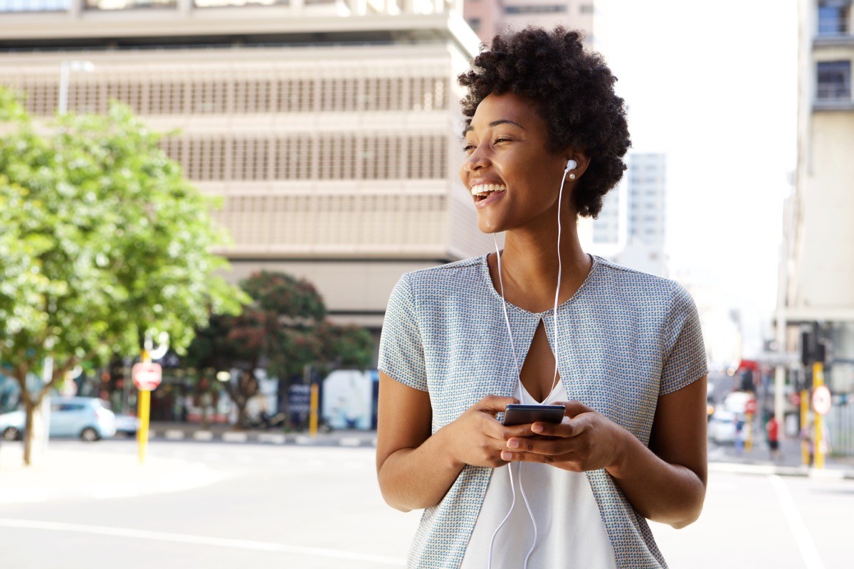A woman walking outside in the sun, listening to music on her phone
