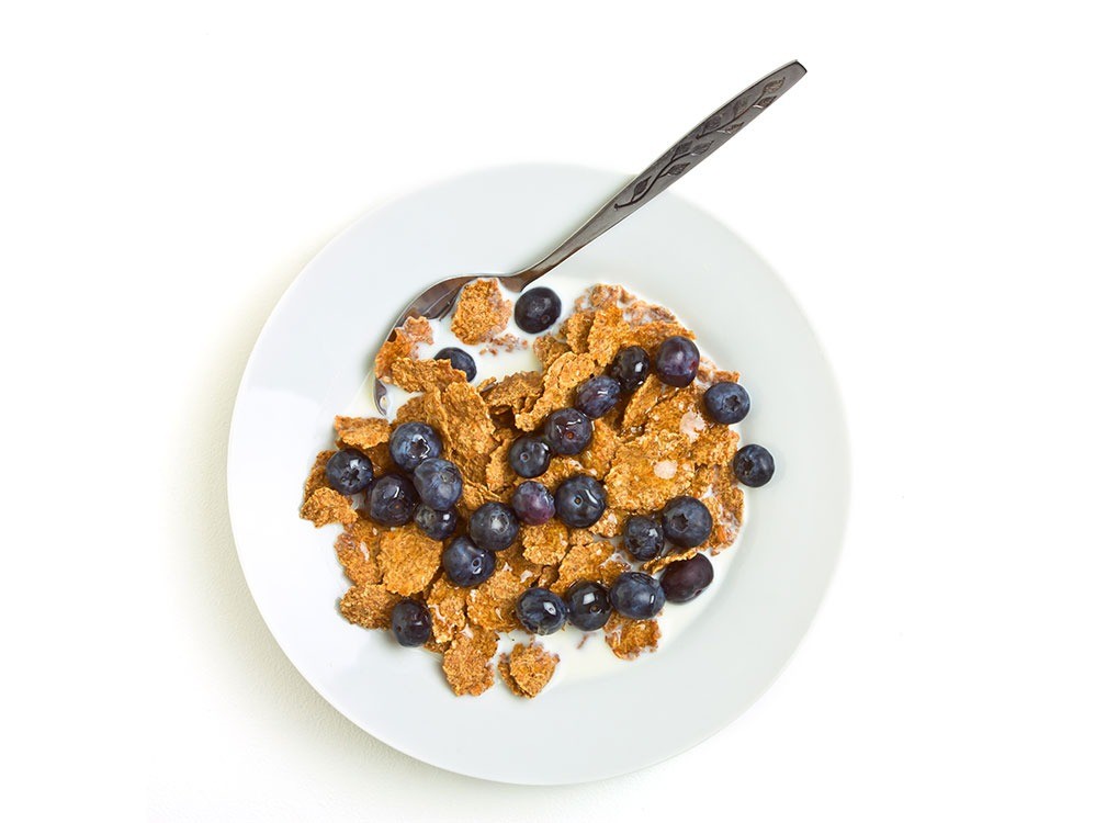 A bowl of whole grain cereal and blueberries on a white backdrop