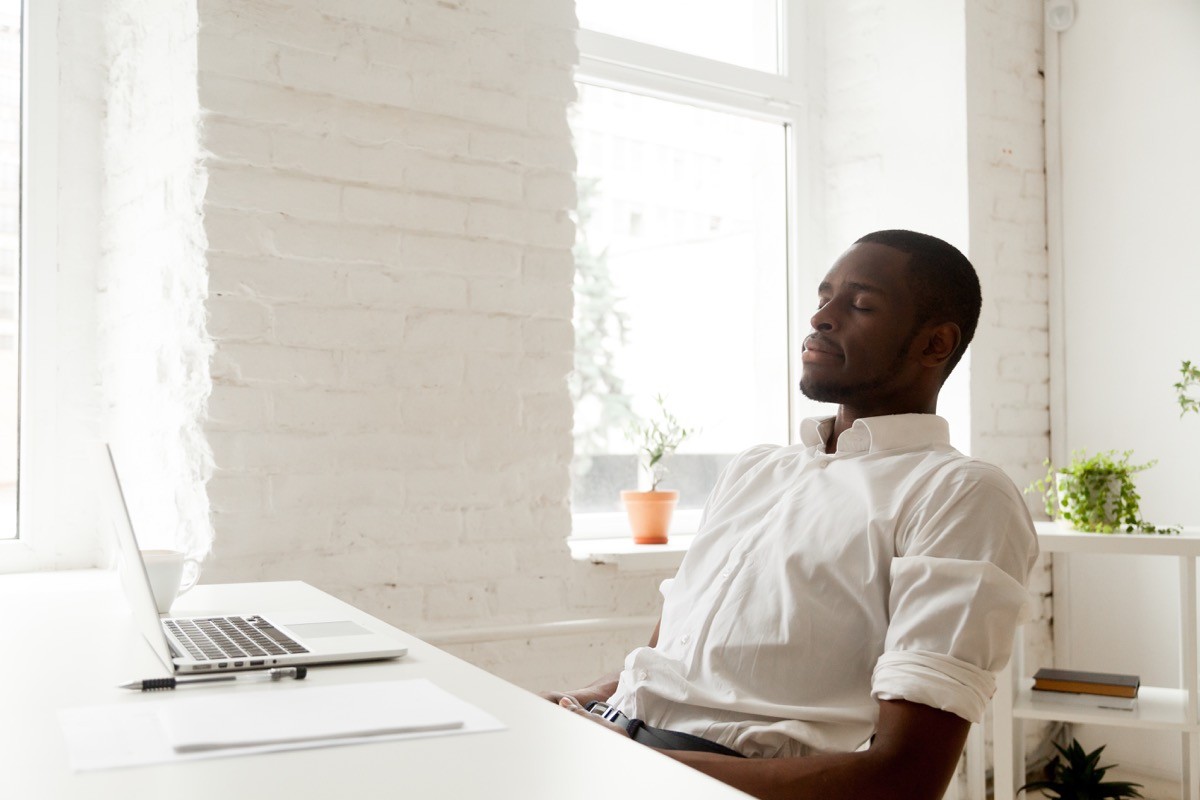 Man taking a deep breath with his eyes closed at his desk