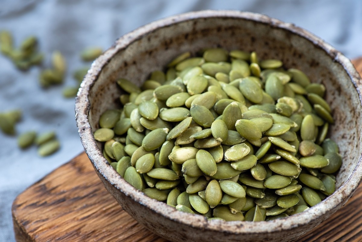 green pepitas, or pumpkin seeds, in a small bowl on a wood cutting board