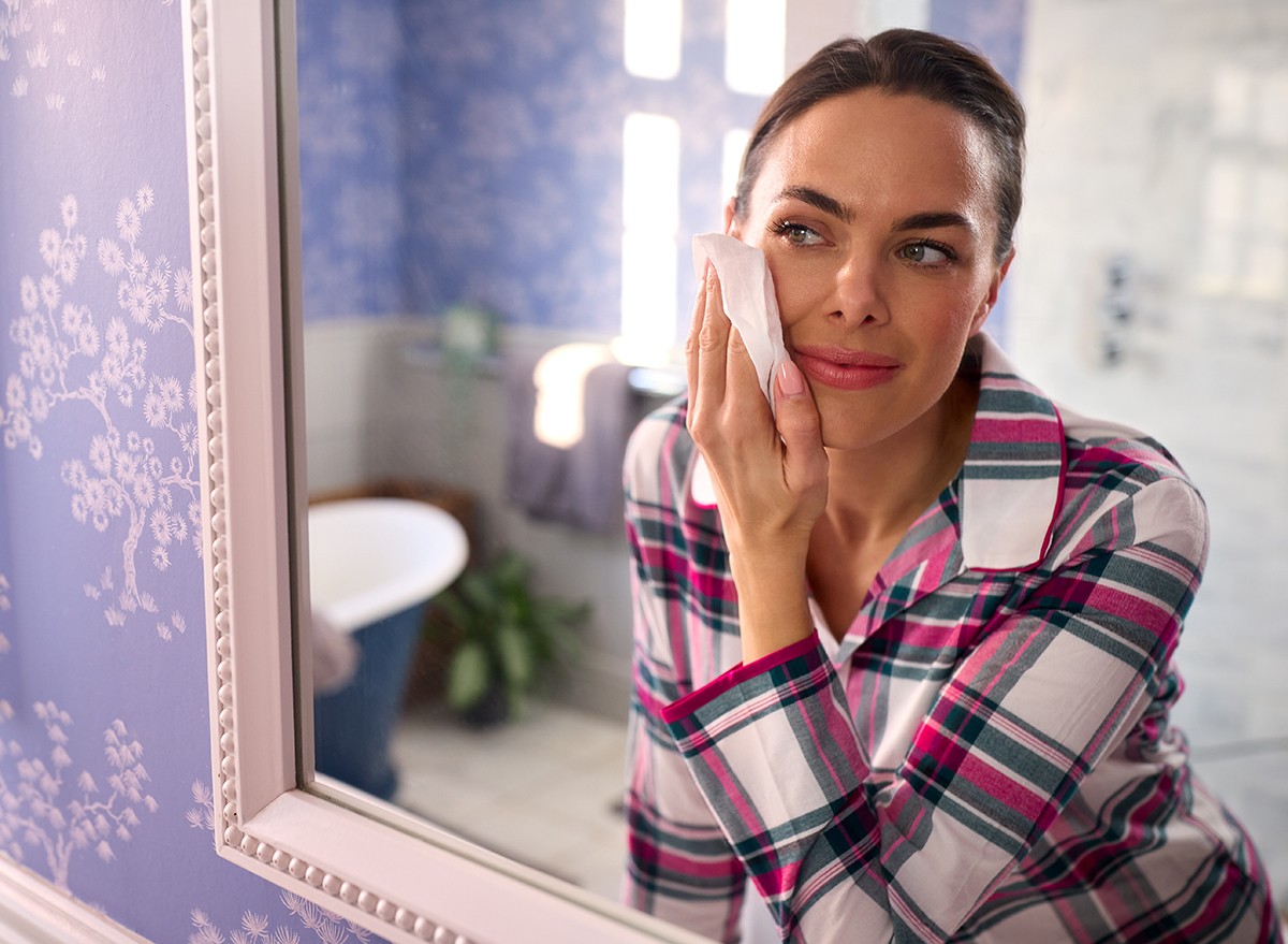 Woman using a face wipe to remove her makeup, looking in the mirror